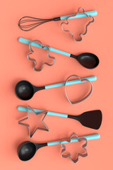 Set of metal cookie cutters and wooden kitchen utensils on coral background