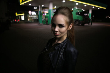 Obraz premium a beautiful fashionable red-haired girl poses at night on the street in the city, in autumn near a gas station