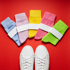 Colorful socks in front of sneakers on red background. Top view