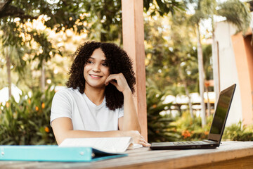 Happy student smiling posing sitting on a chair in a desk in a campus.