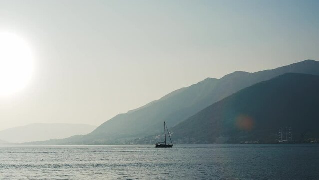 Silhouette of a sailboat against the background of the bay of the sea and mountains, at sunrise. A concept for travel, vacation, freedom, friends