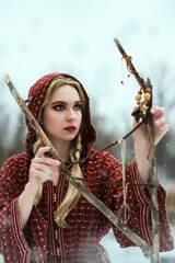 Bright color photo of a beautiful sorcerer girl with blond braids in a winter forest next to a...