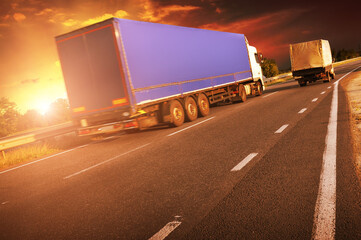 Big truck with a trailer on a road with other truck against a sky with a sunset - 546998081