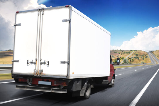 Big white box truck on a road in motion against a sky with clouds