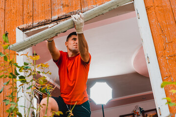 A worker dismantles an old window in the house with a crowbar.