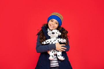 smiling child in puffer jacket hold toy. teen girl on red background. happy childhood.