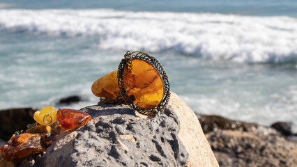 Transparent orange Baltic old pendant near the sea. Beautiful natural amber jewelry on the rock. 