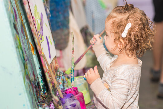 Toddler girl during art project. Kid holds paintbrush. Baby paints with brush on a paper. A girl paints a picture
