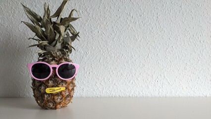 Pineapple in pink glasses on a light background
