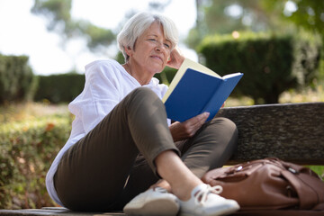 retired woman reading a book on the bench