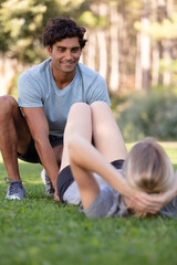 Naklejka premium smiling woman with personal trainer doing exercises on mat outdoors