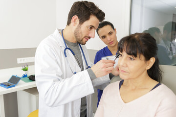Obraz na płótnie Canvas doctor holding otoscope and examining ear of senior woman