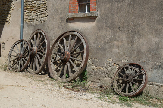 Four old wooden wheels with metal strapping, designed for hay and straw transport carts in the countryside. Different diameters, against a farm wall