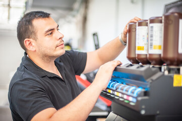 In the printing house, an experienced technician works on a UV printer. Production work. Check the print quality.