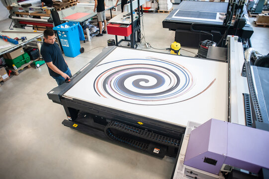 In the printing house, an experienced technician works on a UV printer. Production work. Check the print quality.