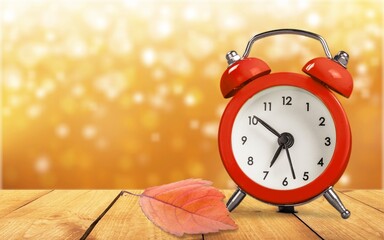 Alarm retro clock with autumn dry leaf on desk