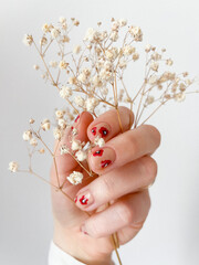 Wiosenny manicure w czerwone maki kwiatki, dłoń trzymająca gipsówkę