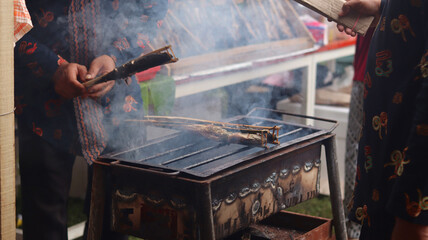 a man who is grilling fish traditionally uses a grill to sell and see the smoke. 