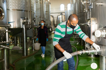 Confident male winegrower working in wine cellar, filtering wine in barrels
