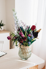 colorful flower bouquet in glass vase on table working space office or at home, sunlight from window, cozy interior, copy space