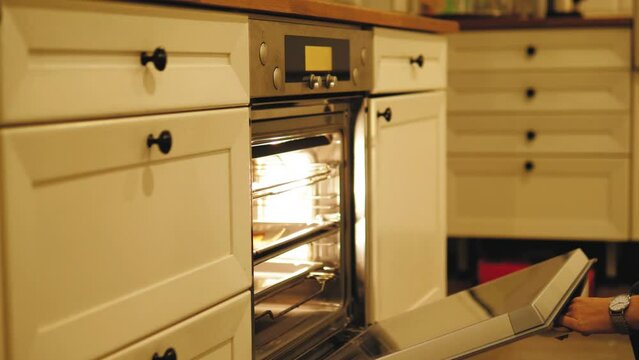 Close up of woman hand opening a modern cooking oven, kitchen utensils. Concept. Details of cooking process, putting a baking dish inside the oven.