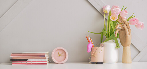 Notebooks with alarm clock, stationery and bouquet of tulips at workplace in office