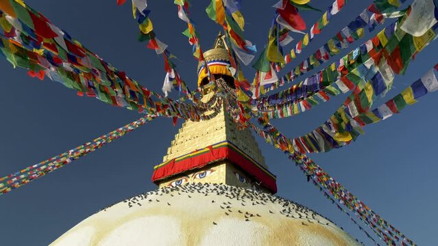Boudhanath stupa in Kathmandu, Nepal. Camera moves between Buddhist flags swaying in the wind, pigeons sit on the dome of Boudhanath Pagoda. UHD, 4K gimbal shot, slow motion