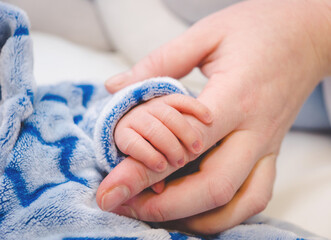 Newborn baby touching his mother hand. Mother uses her hand to hold her baby's tiny hand to make him feeling her love, warm and secure. Concept of child care, feeling safe, parent love.