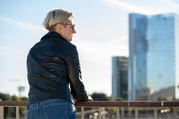 30s woman from the back with short blonde hair in leather jacket in the city with skyscraper on background. Barcelona, Spain