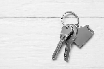 Metal keys with house shaped keychain on white wooden background