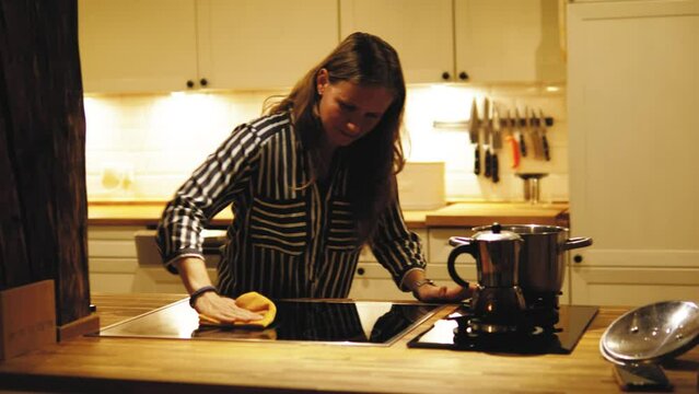 Young woman girl cleaning kitchen, wiping oven in the evning or night. Hardworking housewife working hard at home, making kitchen clean and tidy 