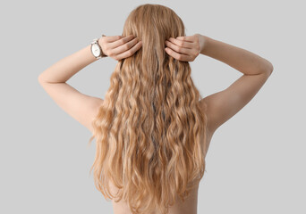 Young blonde woman touching curly hair on light background