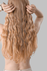 Fototapeta premium Young blonde woman touching curly hair on light background