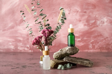 Obraz premium Cosmetic dropper bottles with rocks and ikebana on pink background