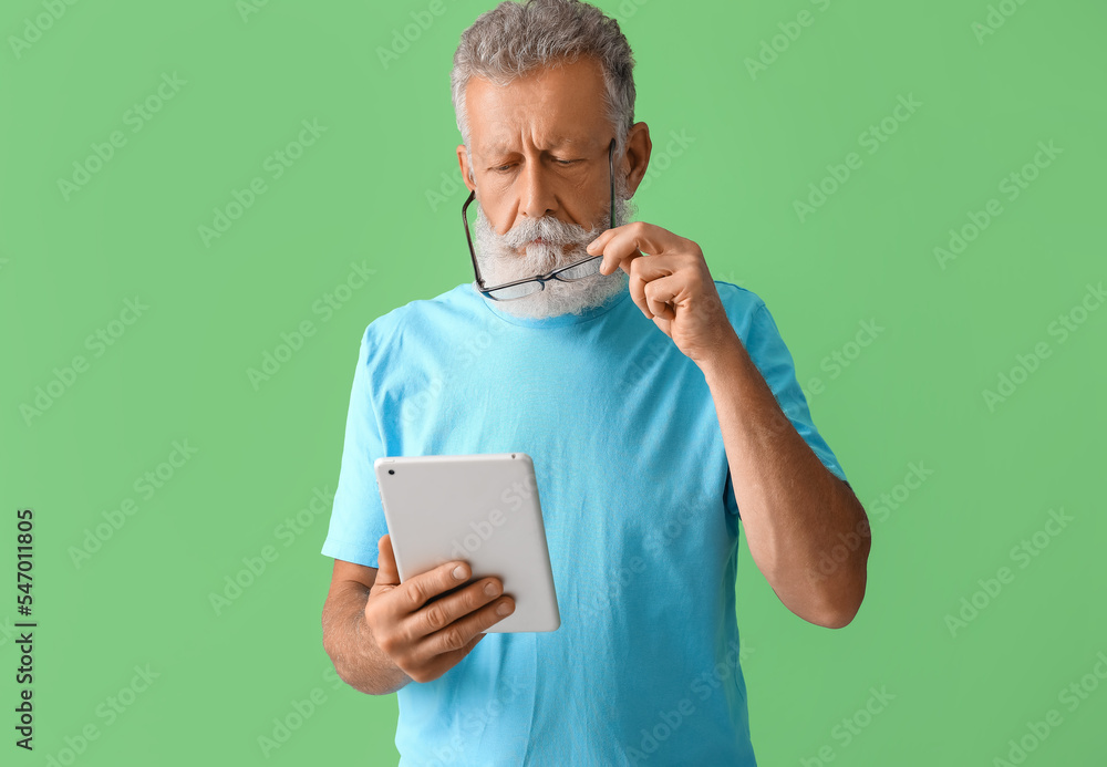 Poster senior man with eyeglasses using tablet computer on green background