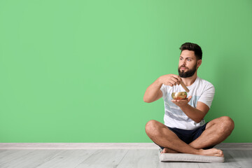 Young man with Tibetan singing bowl sitting near green wall