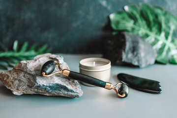 Black gua sha roller on a stone and a candle with greenery