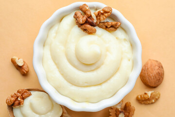 Ramekin of tasty vanilla pudding with walnuts on color background, closeup