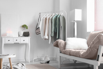 Interior of light living room with rack, sweaters and couch