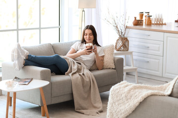Young woman with glass cup of cocoa lying on grey sofa in kitchen