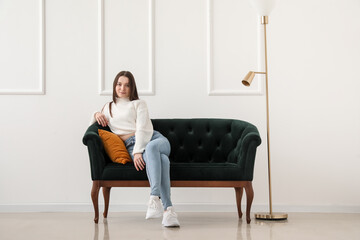 Young woman sitting on green sofa near light wall