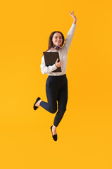 Young assistant with clipboard jumping on yellow background