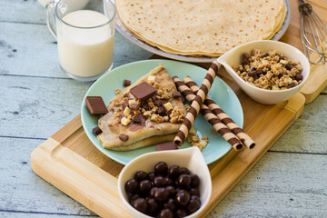 Crepes with chocolate on cutting board with ingredients. Rustic wooden background