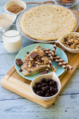 Crepes with chocolate on cutting board with ingredients. Rustic wooden background
