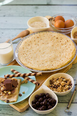 Crepes with chocolate on cutting board with ingredients. Rustic wooden background