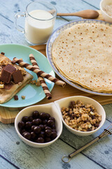 Crepes with chocolate on cutting board with ingredients. Rustic wooden background