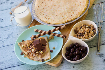 Crepes with chocolate on cutting board with ingredients. Rustic wooden background