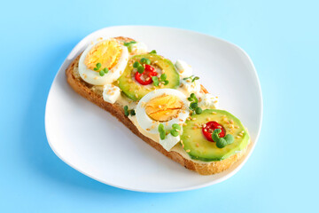 Plate of tasty toast with boiled egg and avocado on color background