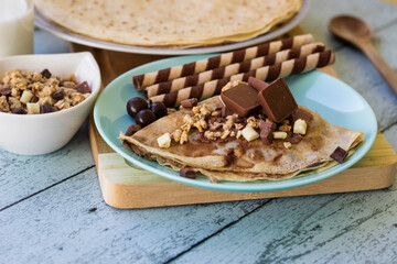 Crepes with chocolate on cutting board with ingredients. Rustic wooden background
