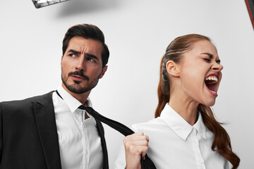 Man and woman pulling on tie anger business looking at each other screaming with hands up in white isolated background. The concept of business in a couple harassment startup copy space